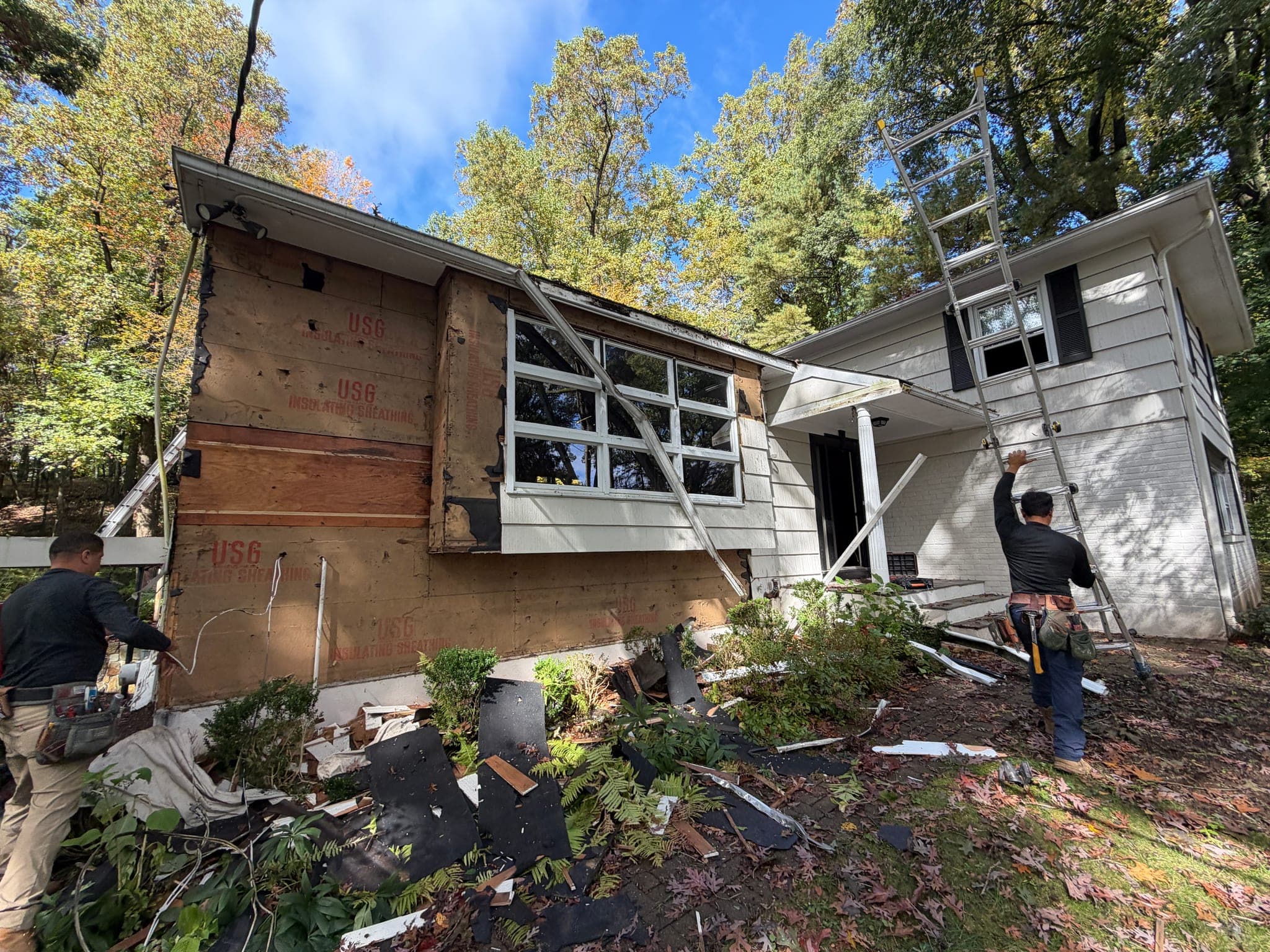 65 Windmill Road: Siding stripped back to the sheathing across the front of the split-level, crew at work